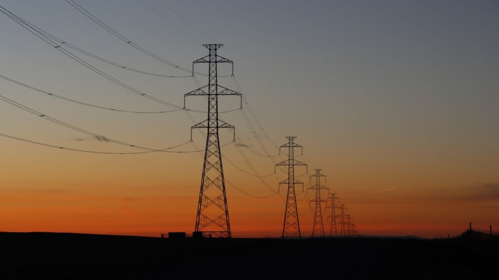 Silhouetted high-voltage power transmission towers against a dramatic sunset sky