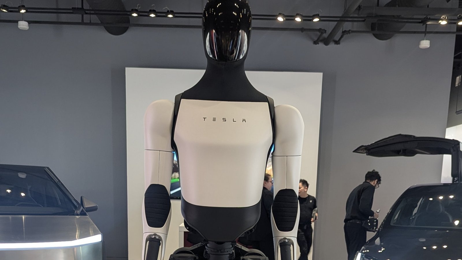 Tesla Optimus humanoid robot on display in a showroom between a Cybertruck and a Model X