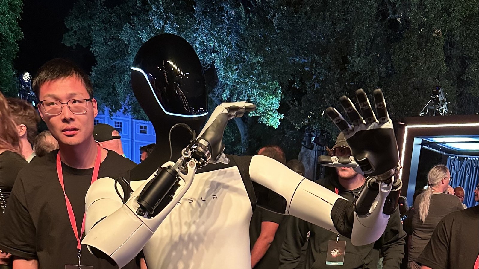 Tesla Optimus humanoid robot waving among the crowd at the Tesla 10/10 event at night