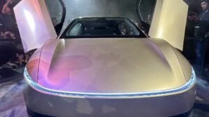 Tesla Cybercab robotaxi at night with its gullwing doors open and the front light bar glowing