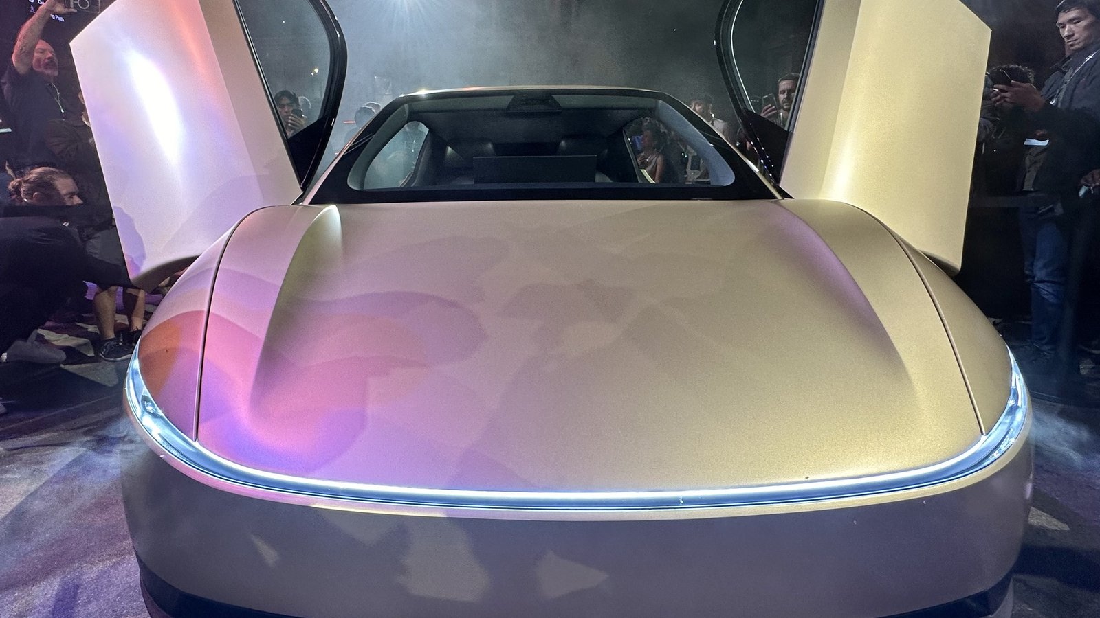 Tesla Cybercab robotaxi at night with its gullwing doors open and the front light bar glowing