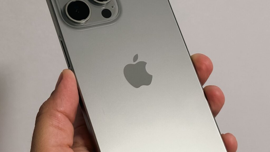 Close-up of a hand holding a silver iPhone Pro with triple cameras