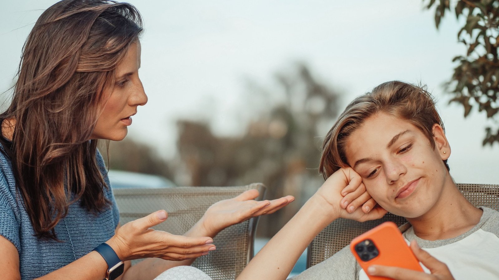 A mother talks to her teenage son as he looks at his smartphone outdoors
